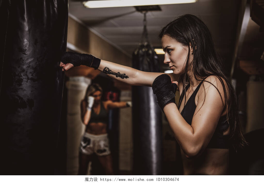 年轻漂亮女子在暗色健身房里用一个拳击袋训练拳击手健身运动拳击